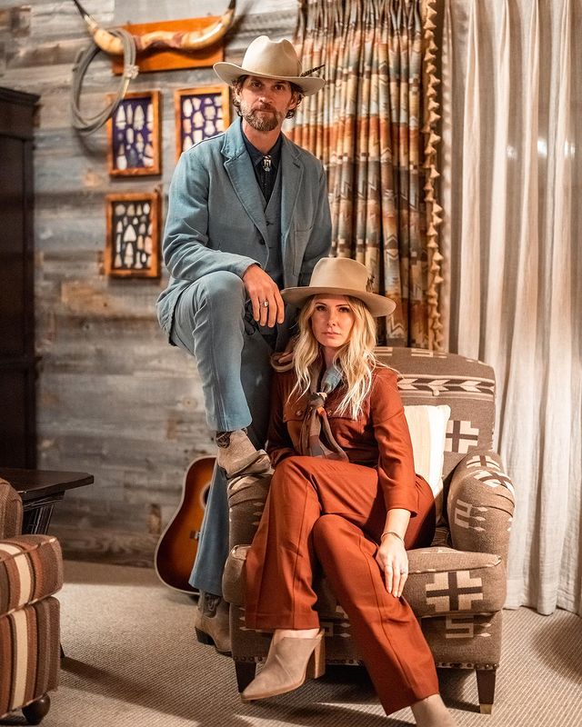 Vanessa Lee Evigan in a bright brown dress posing with her husband in a blue designer dress with nude hats.